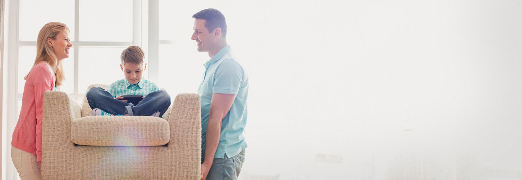 Mother and father moving couch with young son sitting on it, smiling